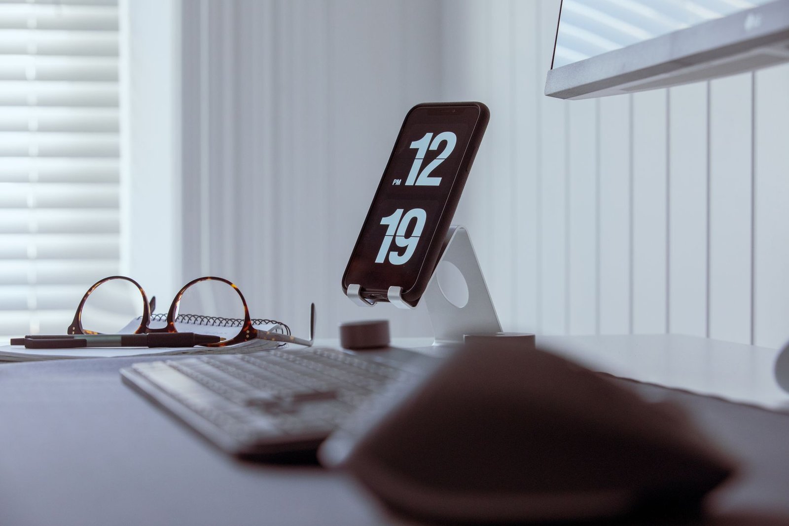 A sleek flip phone resting on a clean wooden work surface next to a notebook.