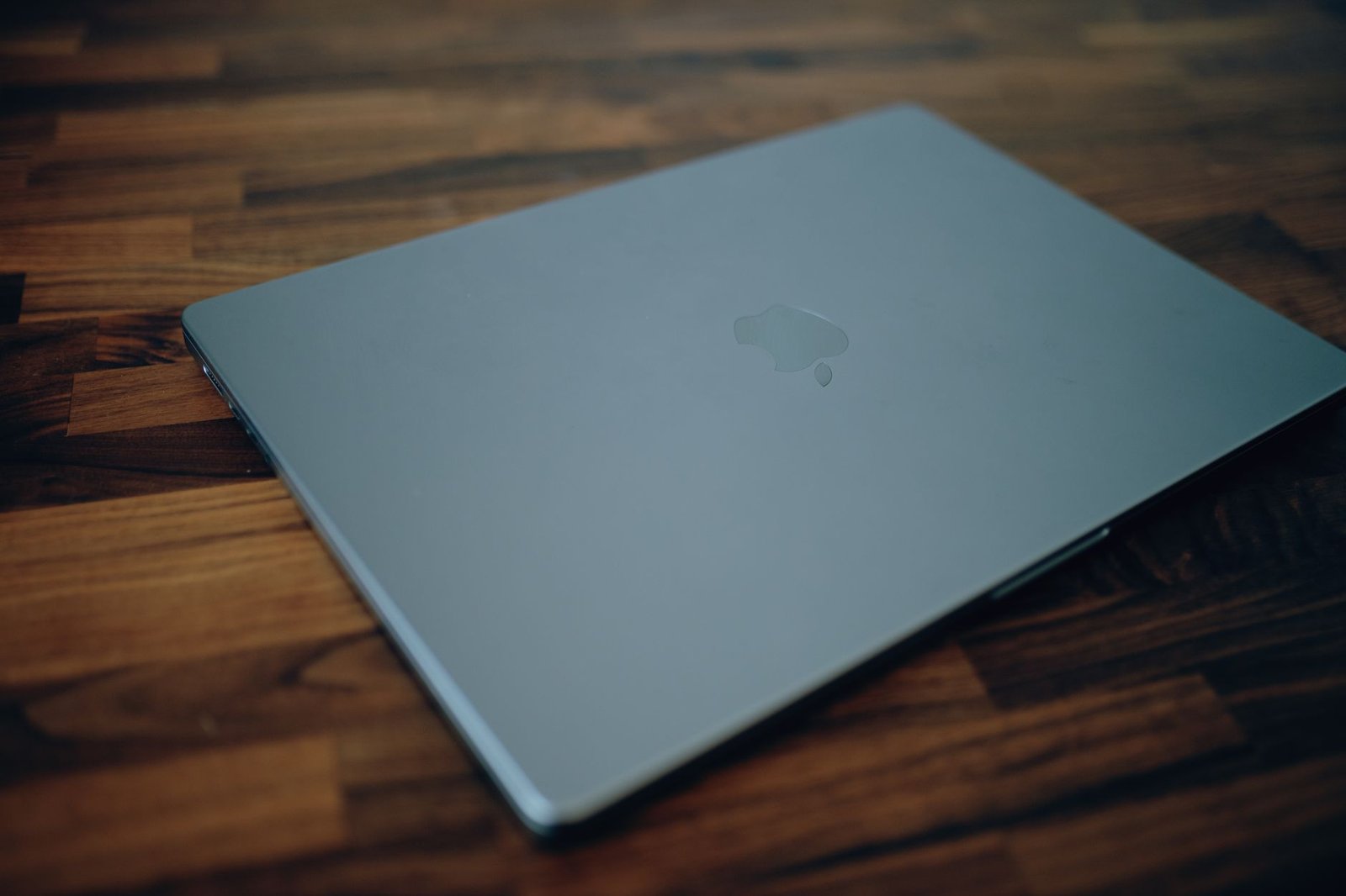 A closed laptop resting neatly on a warm wooden desk at the end of the day.