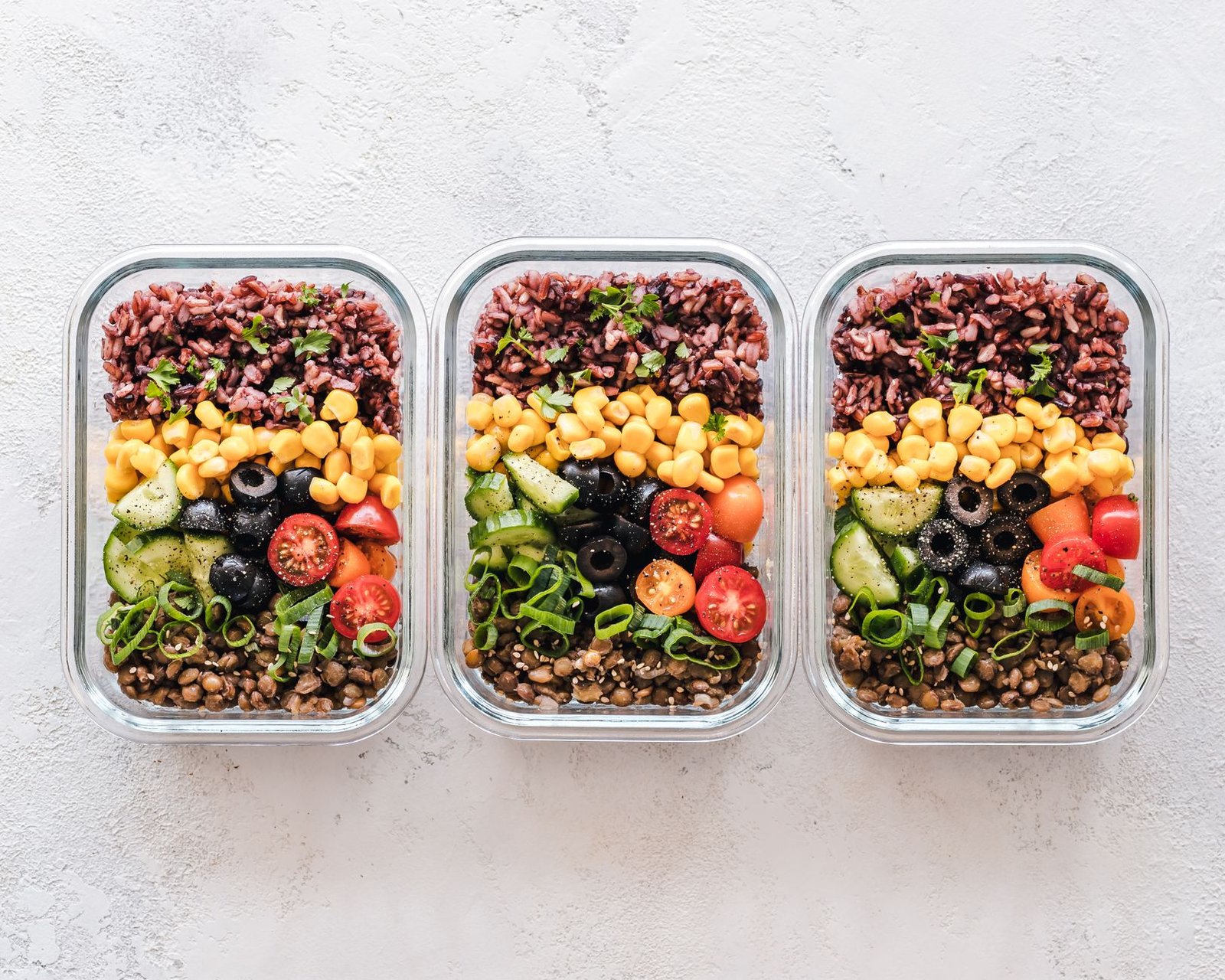 A glass container filled with salmon, avocado, quinoa, and greens.